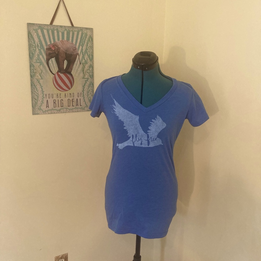 Blue v neck tee with bird. It reads “fly free”